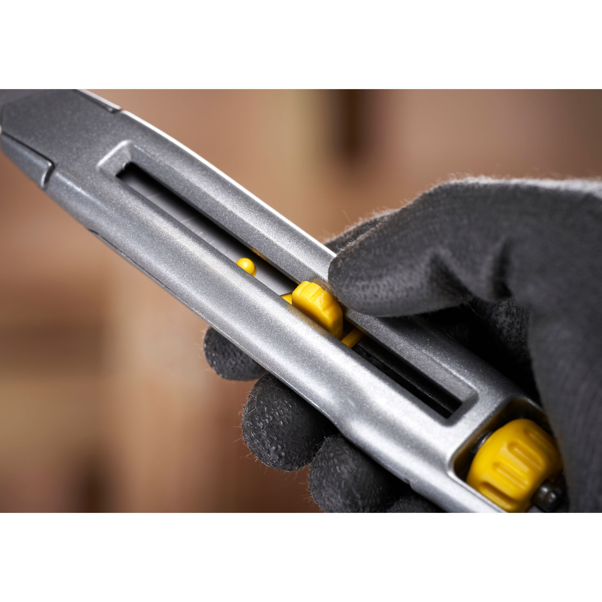 STANLEY 0-10-018 utility knife close-up, showing yellow slider and gloved hand holding the tool.