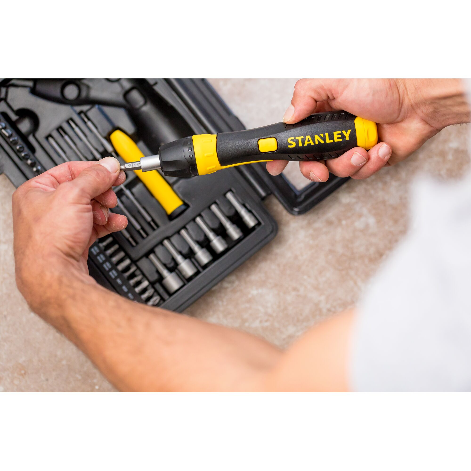 STANLEY 0-63-038 ratcheting screwdriver set with black and yellow handle, person inserting bit, top view.