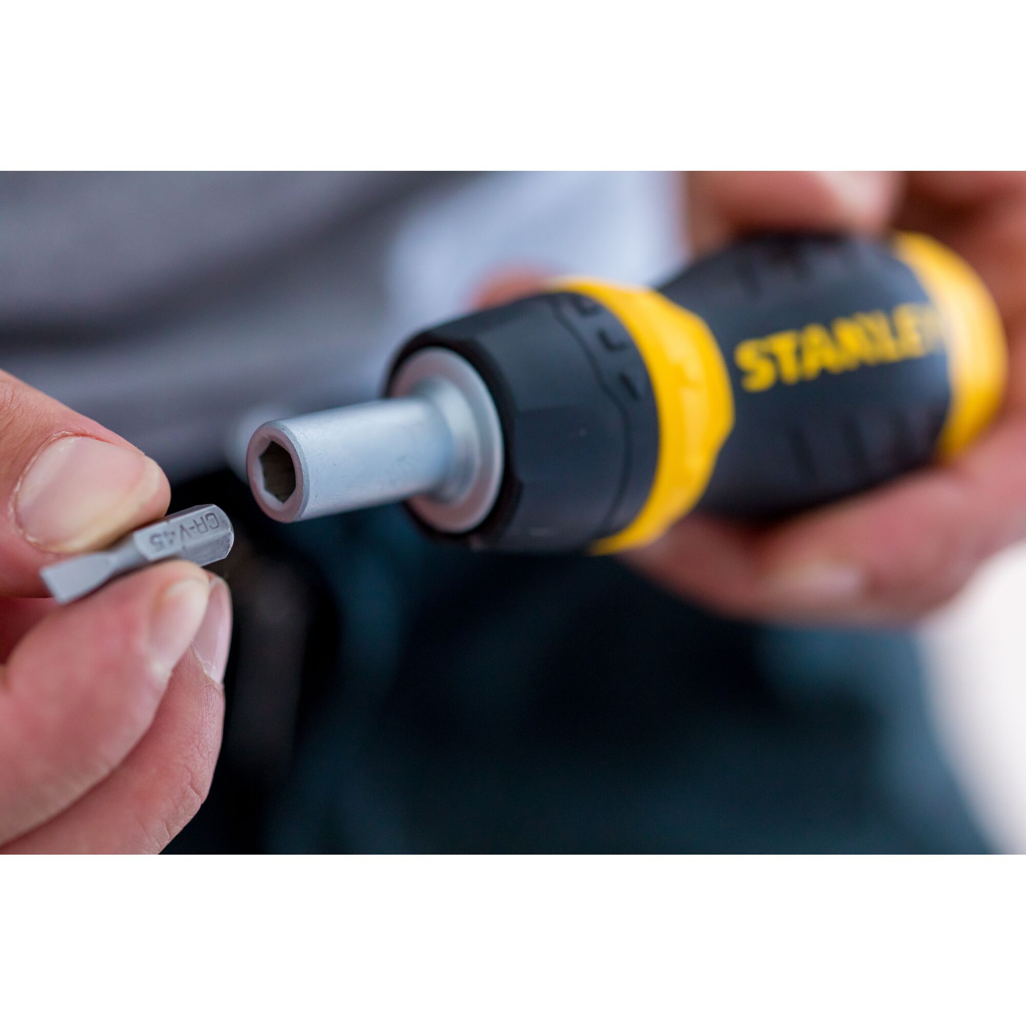 Stanley 0-66-358 screwdriver handle with yellow and black grip, user inserting bit, close-up photo.