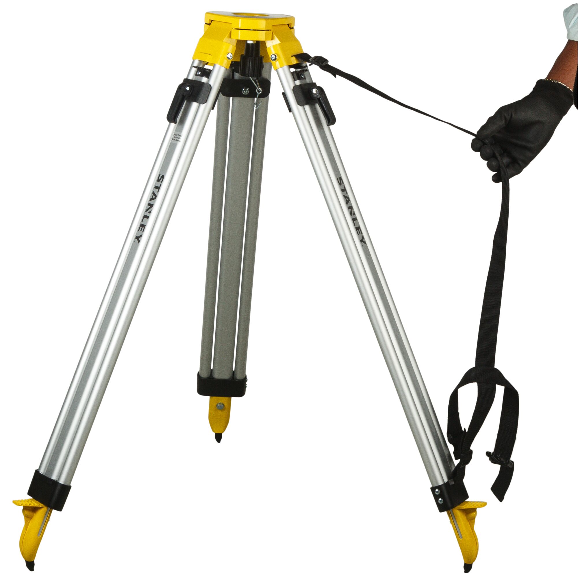 Stanley tripod with yellow head, silver legs, and strap held by a gloved hand, used for photography or surveying.