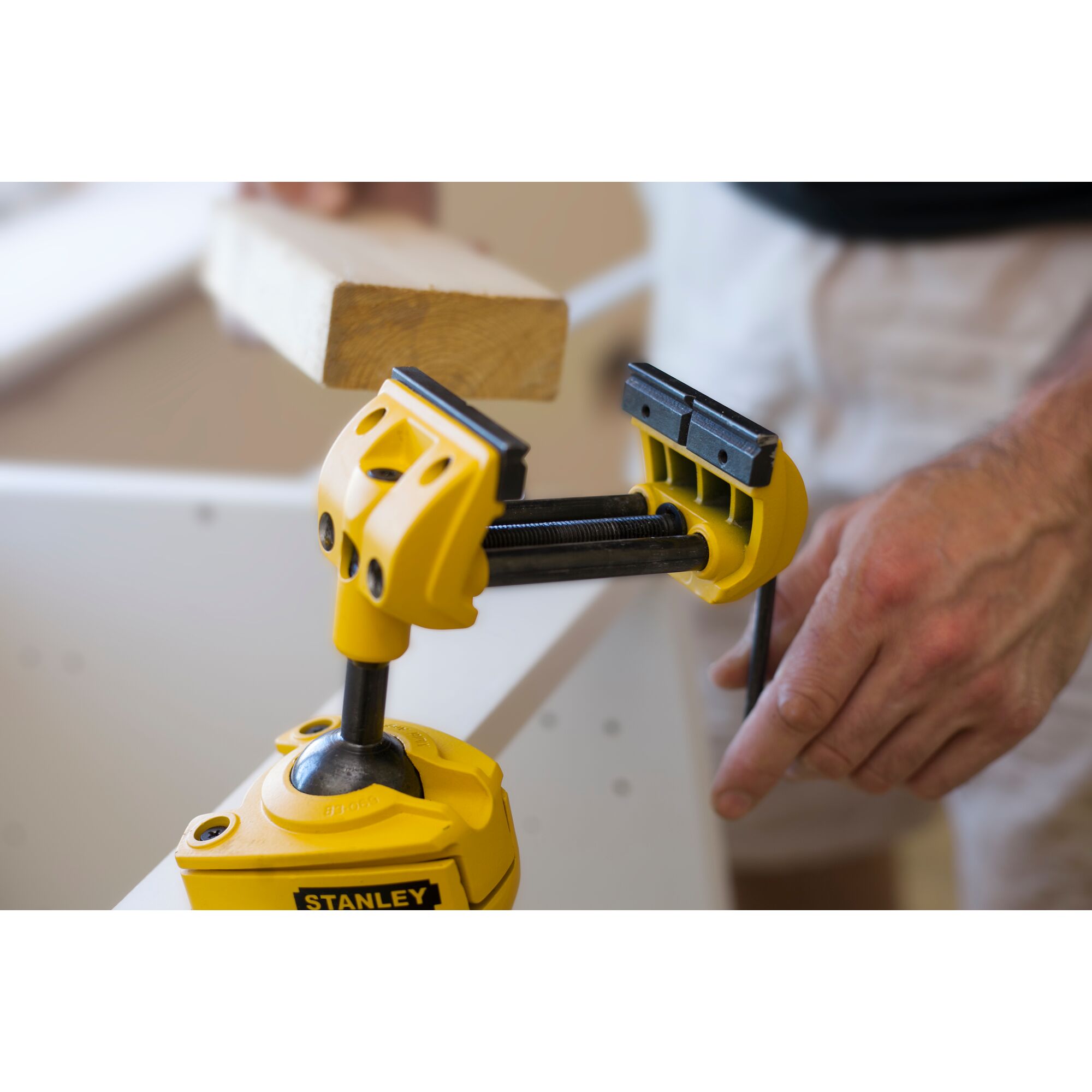 Stanley 1-83-069 adjustable yellow vise clamp holding wood, used in carpentry, close-up photography.