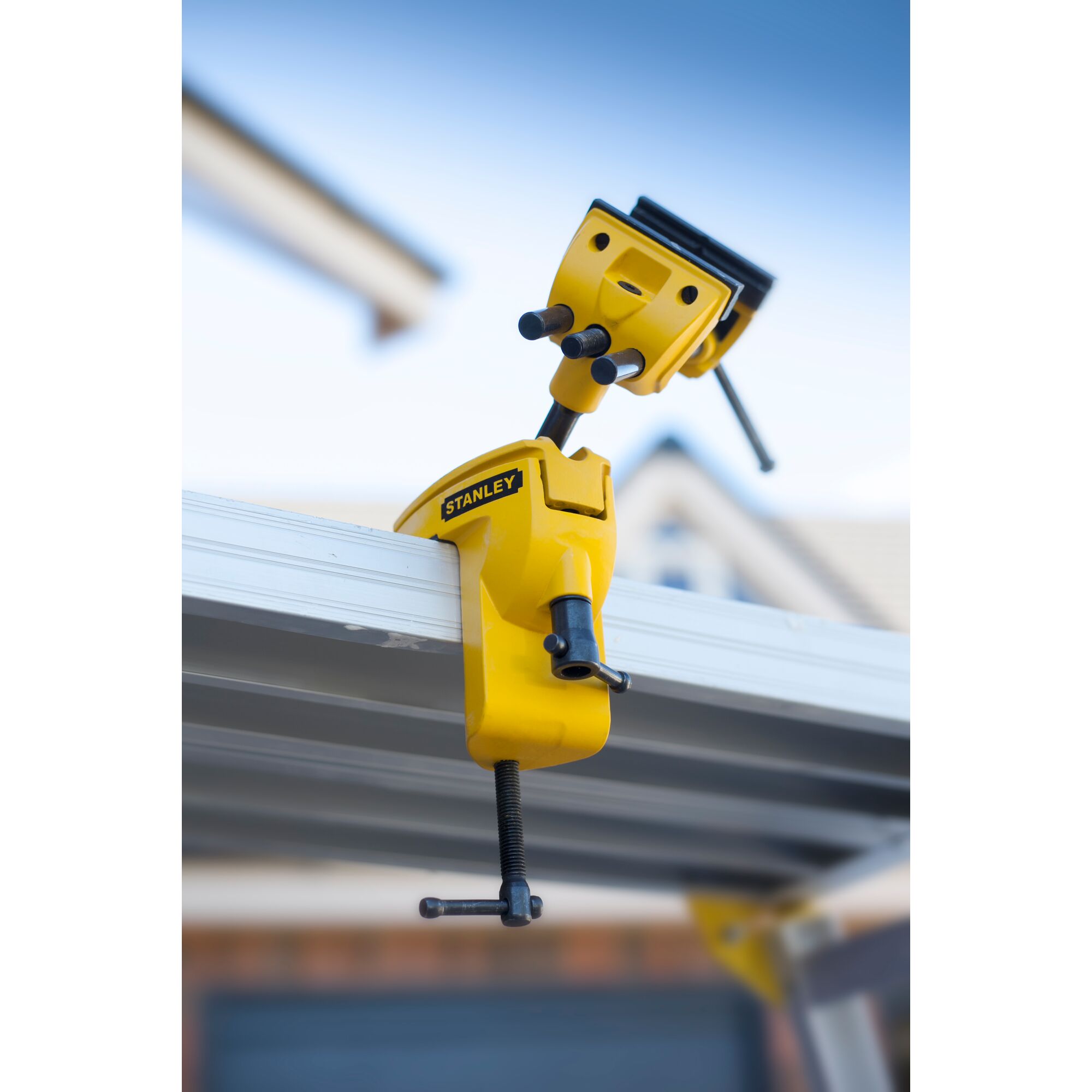 STANLEY 1-83-069 adjustable yellow metal vise clamped to a workbench, side angle outdoor photo.