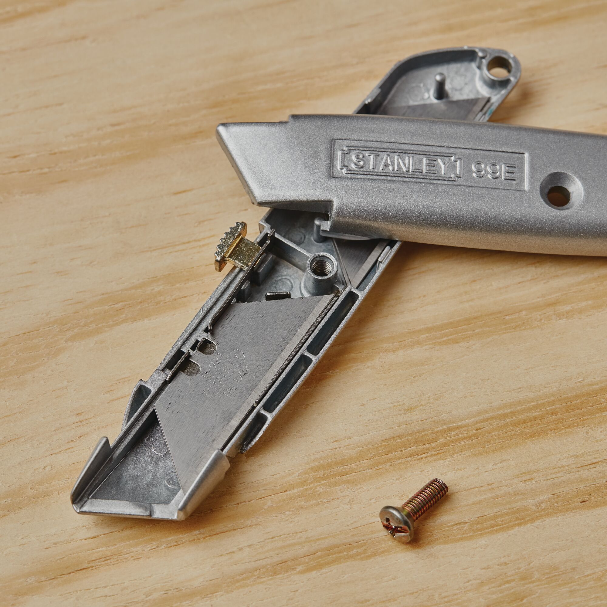 Photo of STANLEY 10-099 utility knife opened with internal parts and screw on wood surface.