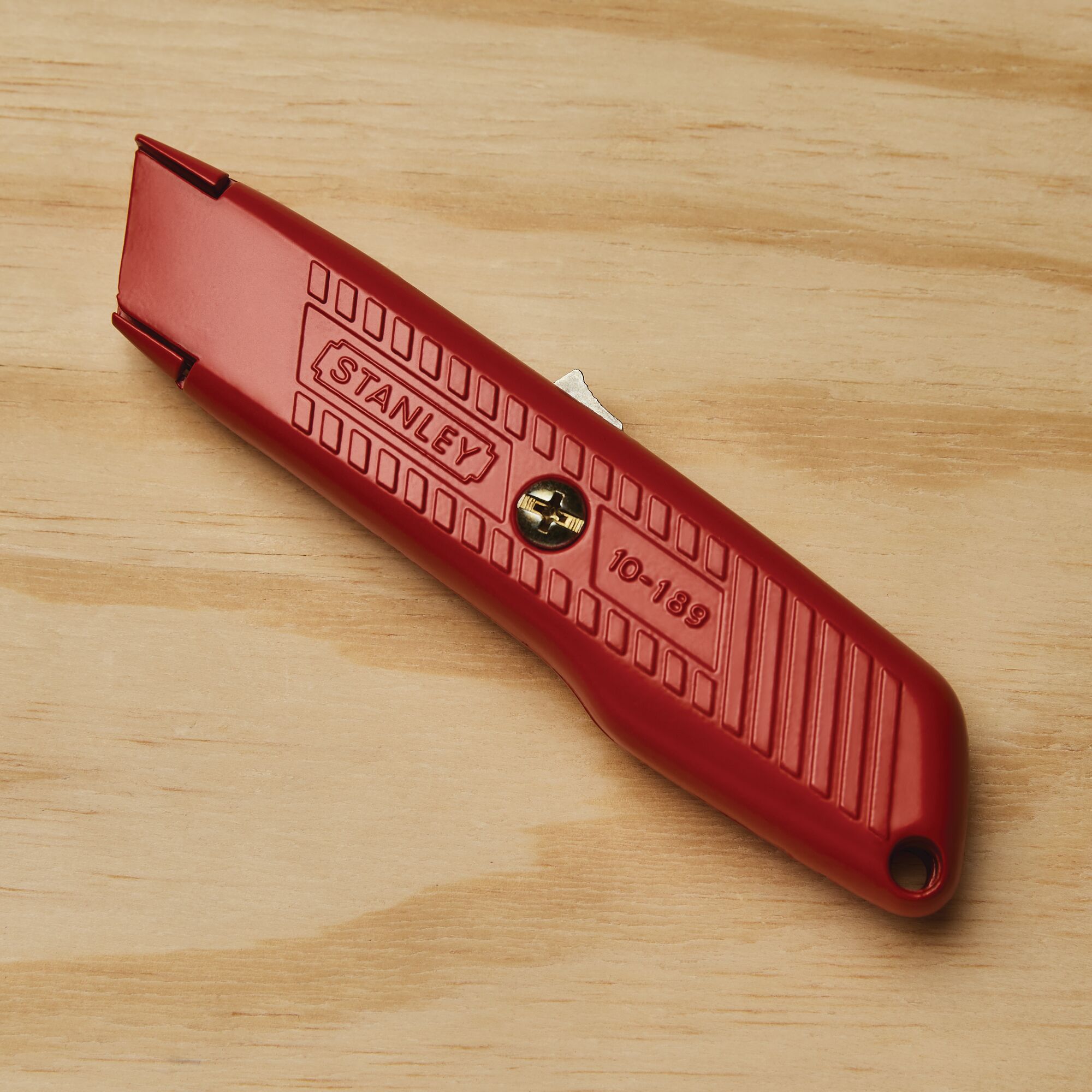 Photo of STANLEY 10-189C red utility knife with textured grip on wood surface.