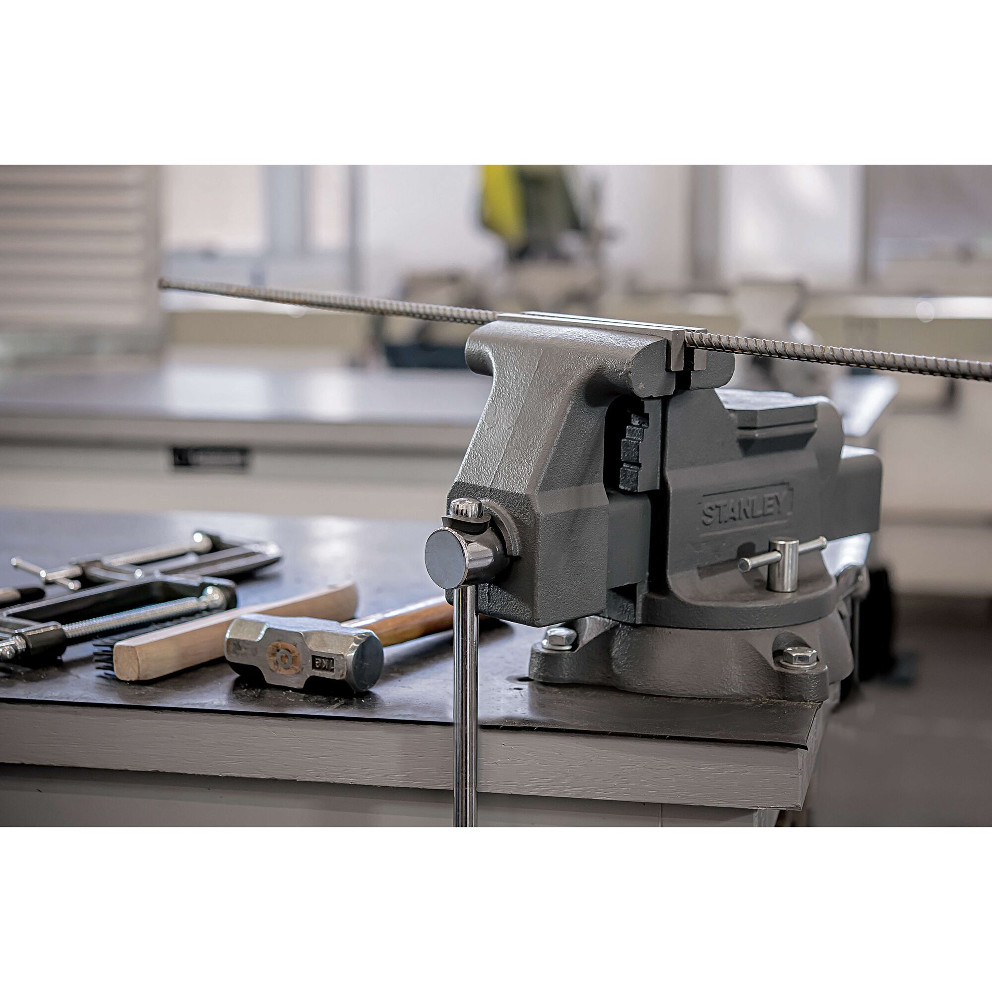 Photo of STANLEY 83-066 bench vise mounted on workbench, holding metal rod, with tools beside it.