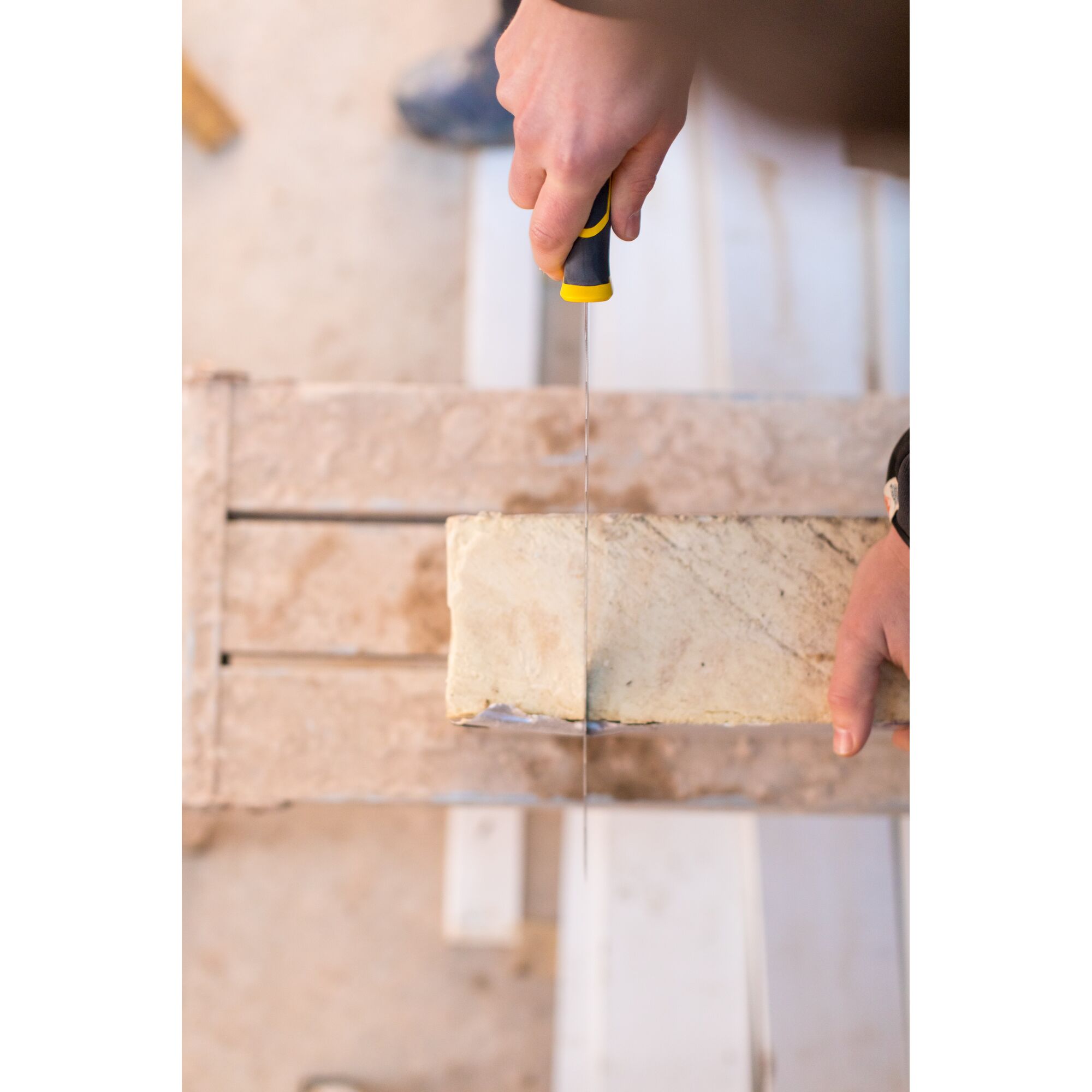 STANLEY FMHT0-10327 hand saw cutting a beige brick, top-down angle, construction setting.