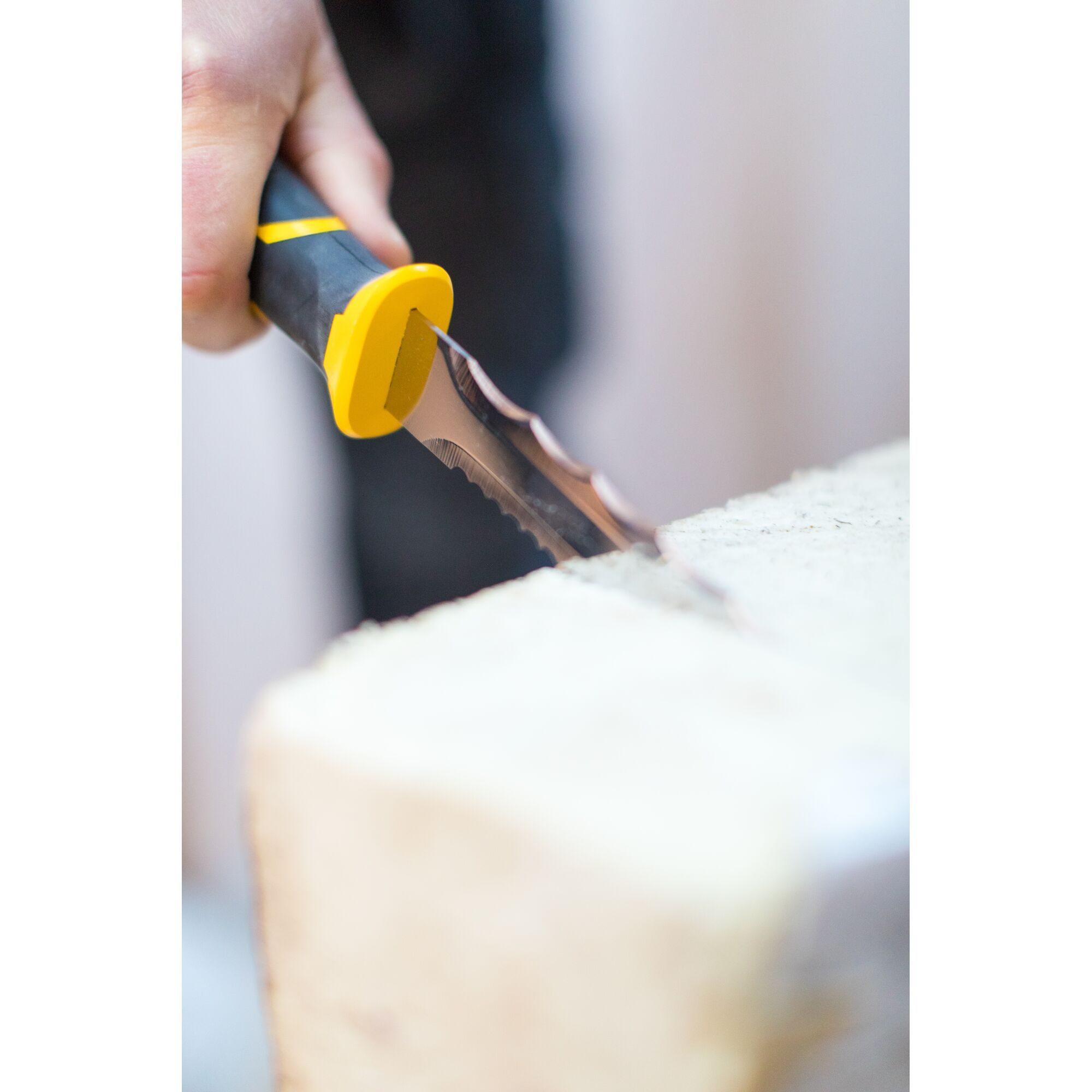 STANLEY FMHT0-10327 serrated blade knife with yellow and black handle cutting light-colored material, close-up.