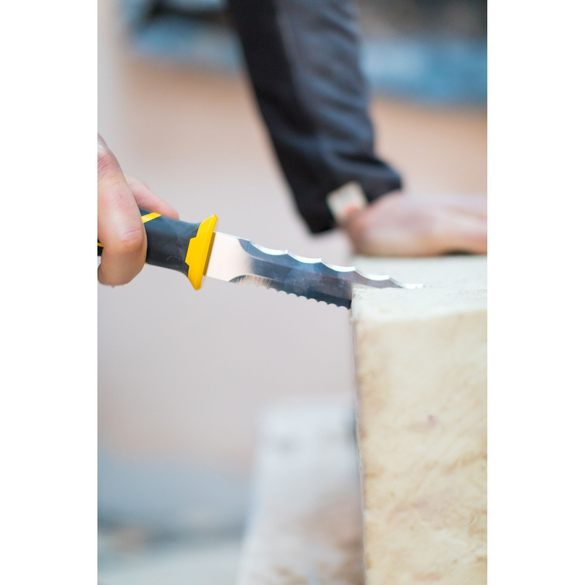 Photo of STANLEY FMHT0-10327 insulation knife with serrated blade cutting yellow insulation material.