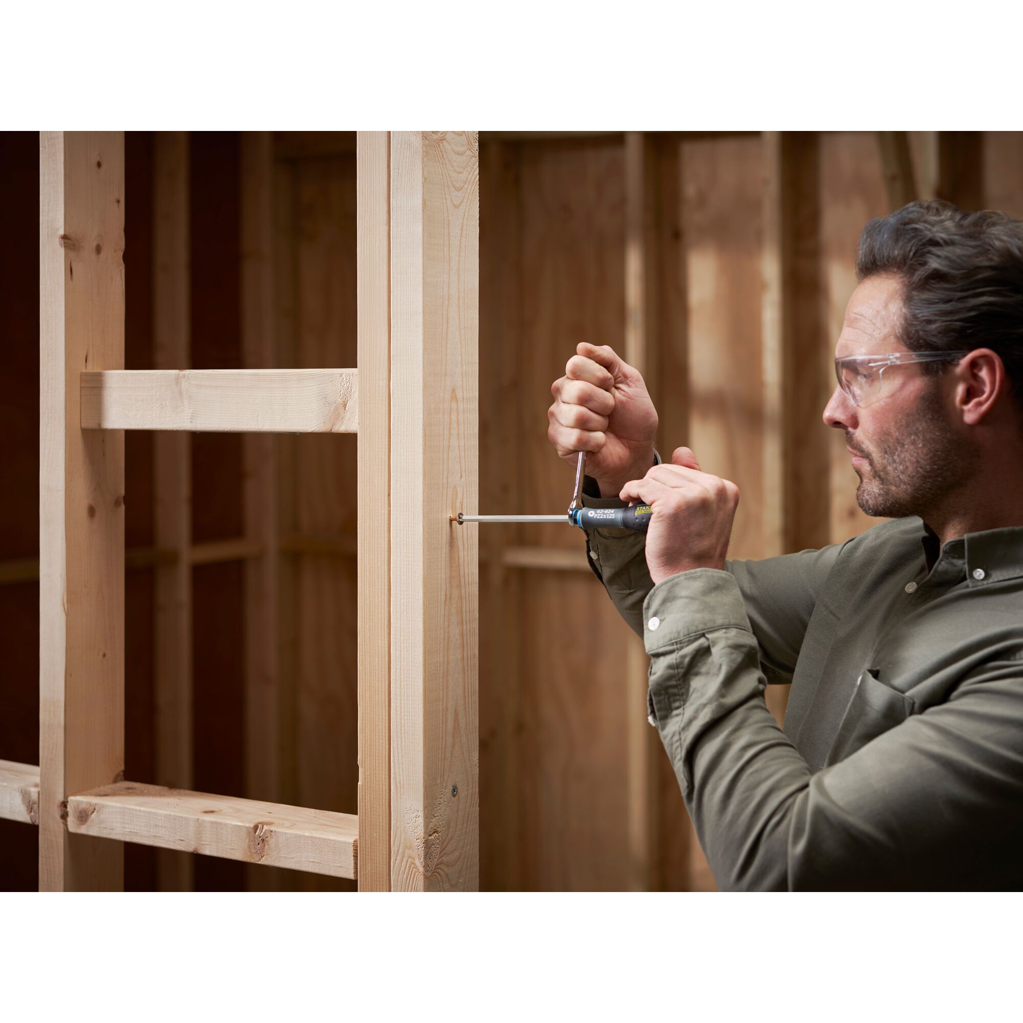 Photo of a person using a STANLEY FMHT0-62624 screwdriver on a wooden frame, construction setting.
