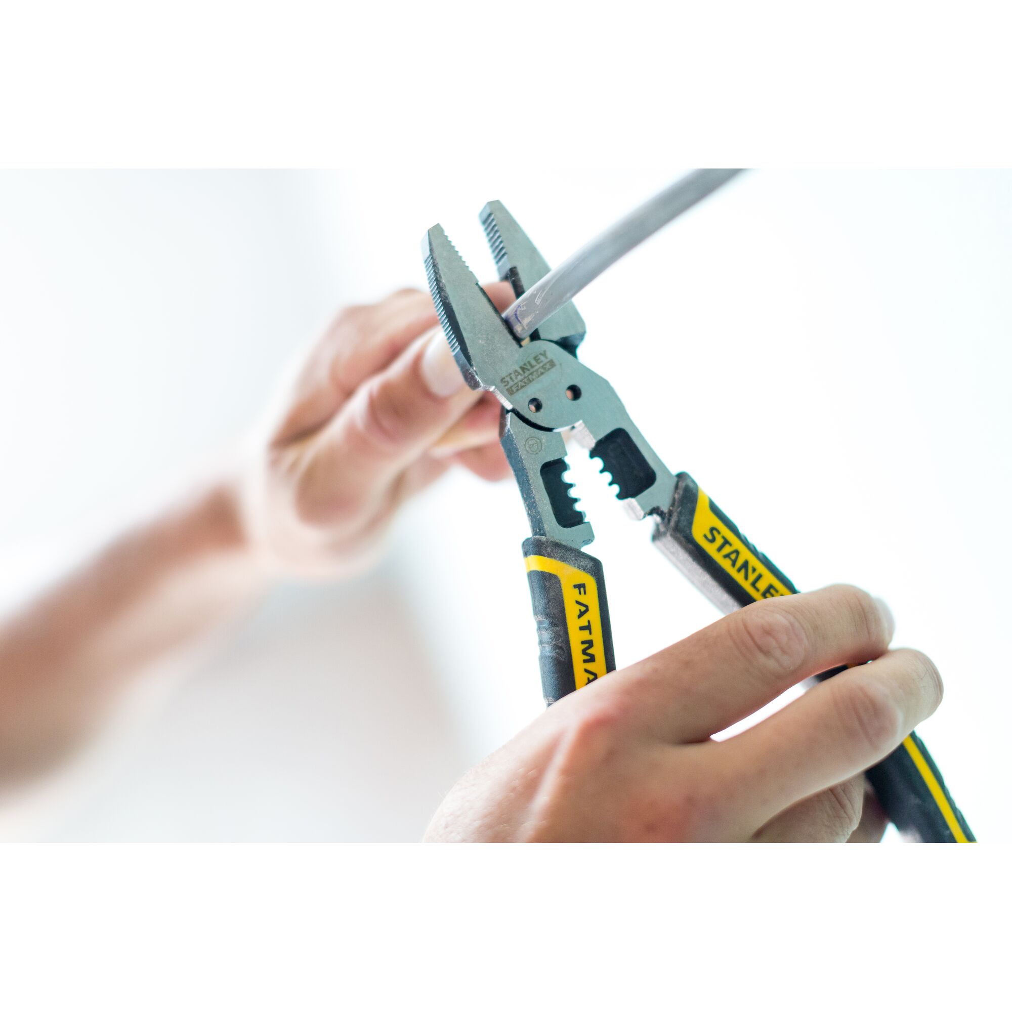 STANLEY FMHT0-75469 pliers gripping wire, close-up photography, black and yellow FATMAX handles.