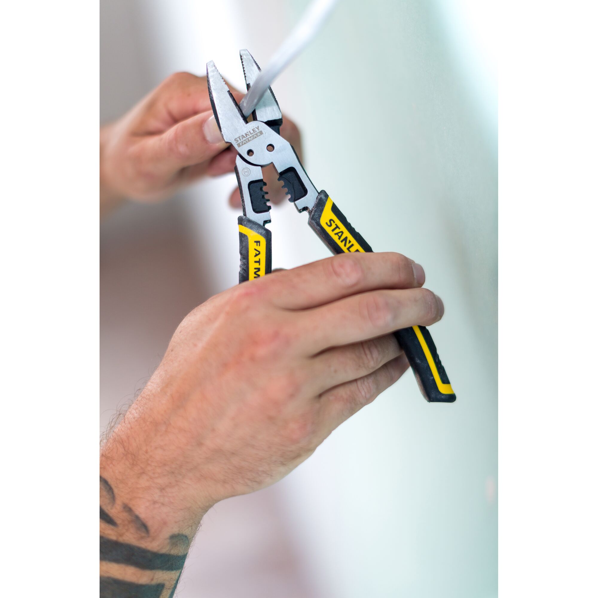 STANLEY FMHT0-75469 wire stripper pliers with black and yellow handles, shown stripping cable in hand, side view.