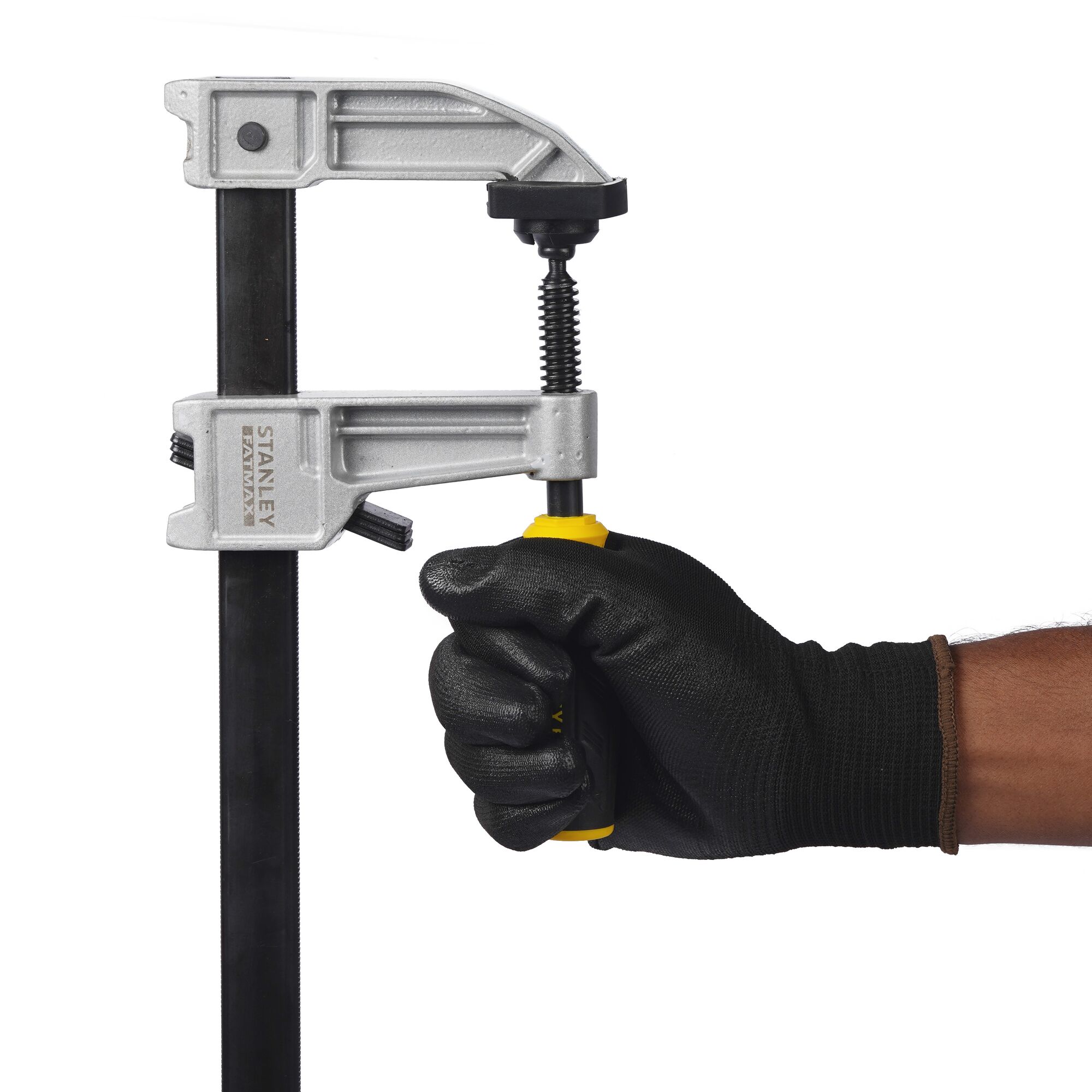 Stanley FMHT0-83247 bar clamp with black and yellow handle held by gloved hand, side view.
