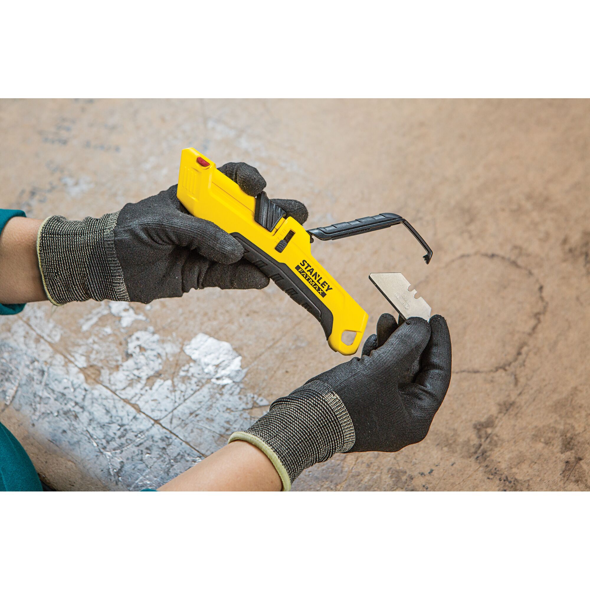 Photo of STANLEY FMHT10365-0 utility knife with yellow handle and blade being replaced by gloved hands.