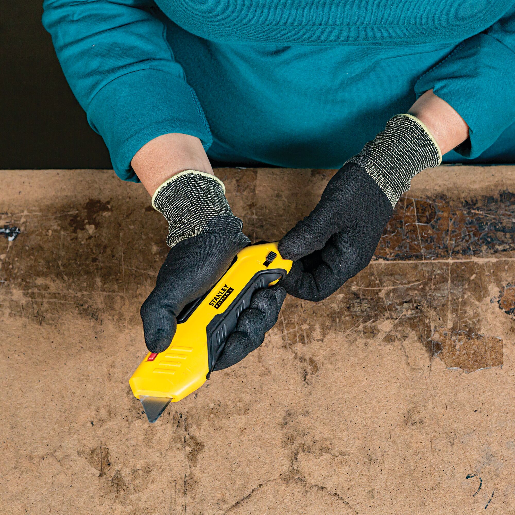 Photo of STANLEY FMHT10369 utility knife held by gloved hands above a workbench, product category: Photography.