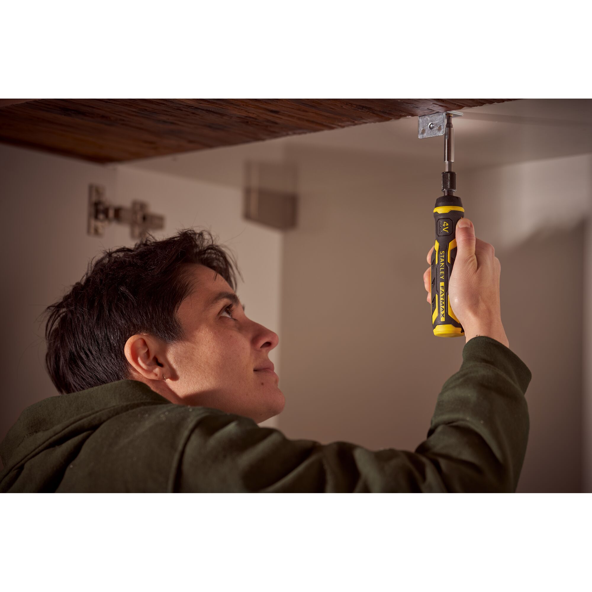 Person using STANLEY FMHT66719-0 ratcheting screwdriver under a wooden cabinet, yellow and black handle visible.
