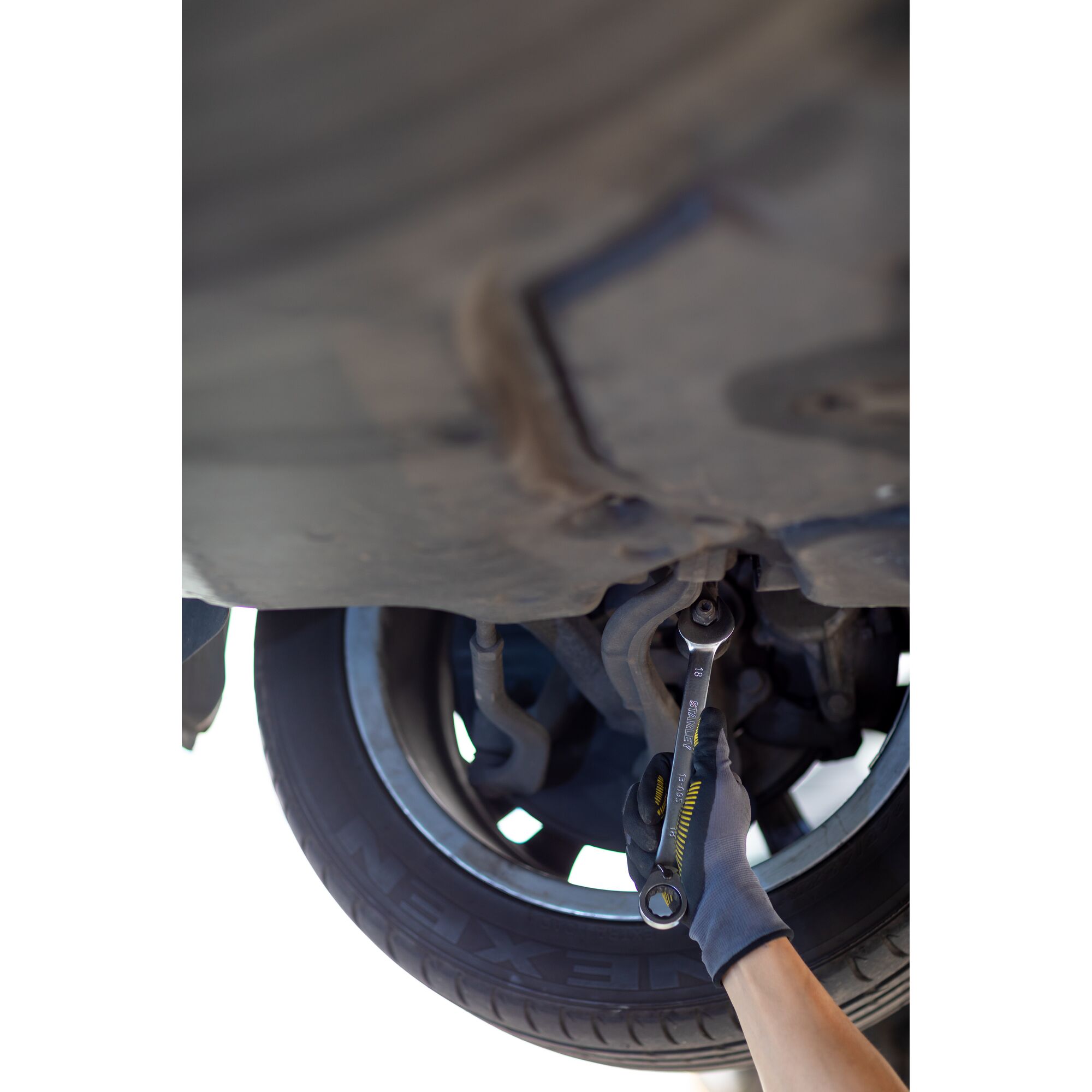 STANLEY FMMT13088-0 ratcheting wrench in use under car near wheel, held by gloved hand.