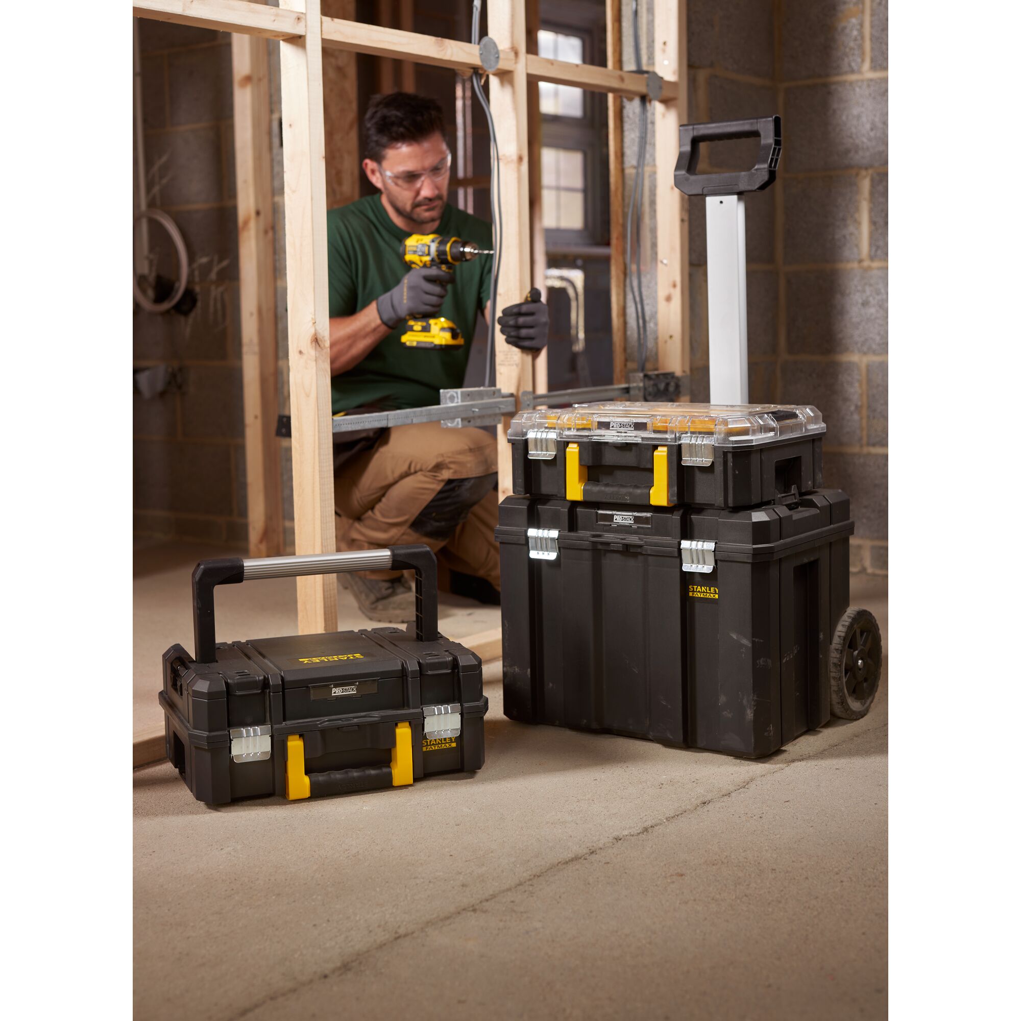 STANLEY FMST1-75753 modular black toolboxes with yellow latches, one on wheels, on a construction site.