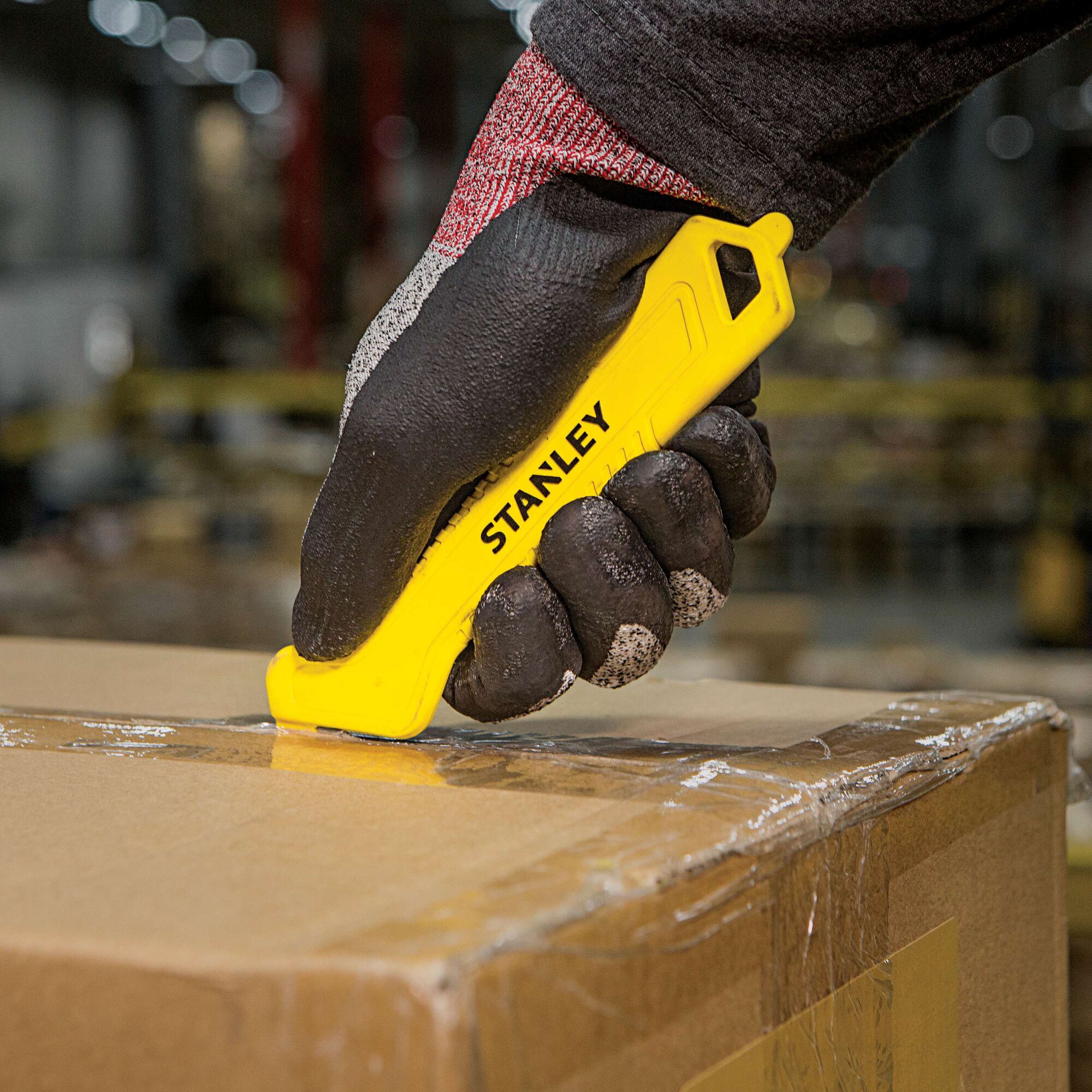 STANLEY STHT10355 yellow safety knife cutting box tape, warehouse setting, closeup photography.