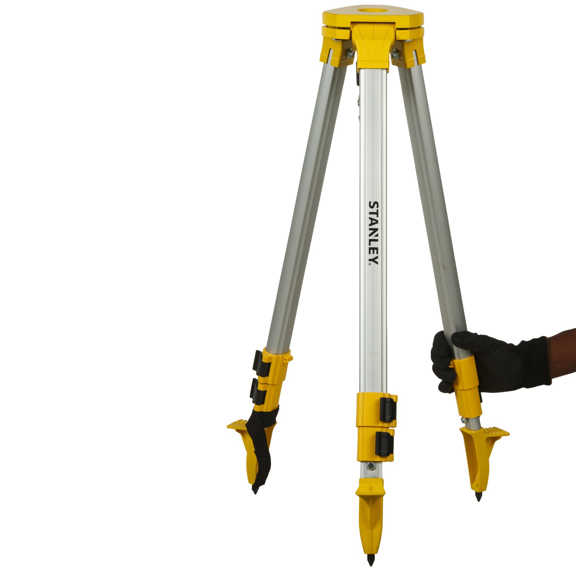 Photo of STANLEY STHT77625-1 photography tripod, silver with yellow joints, angled view, being held by a gloved hand.