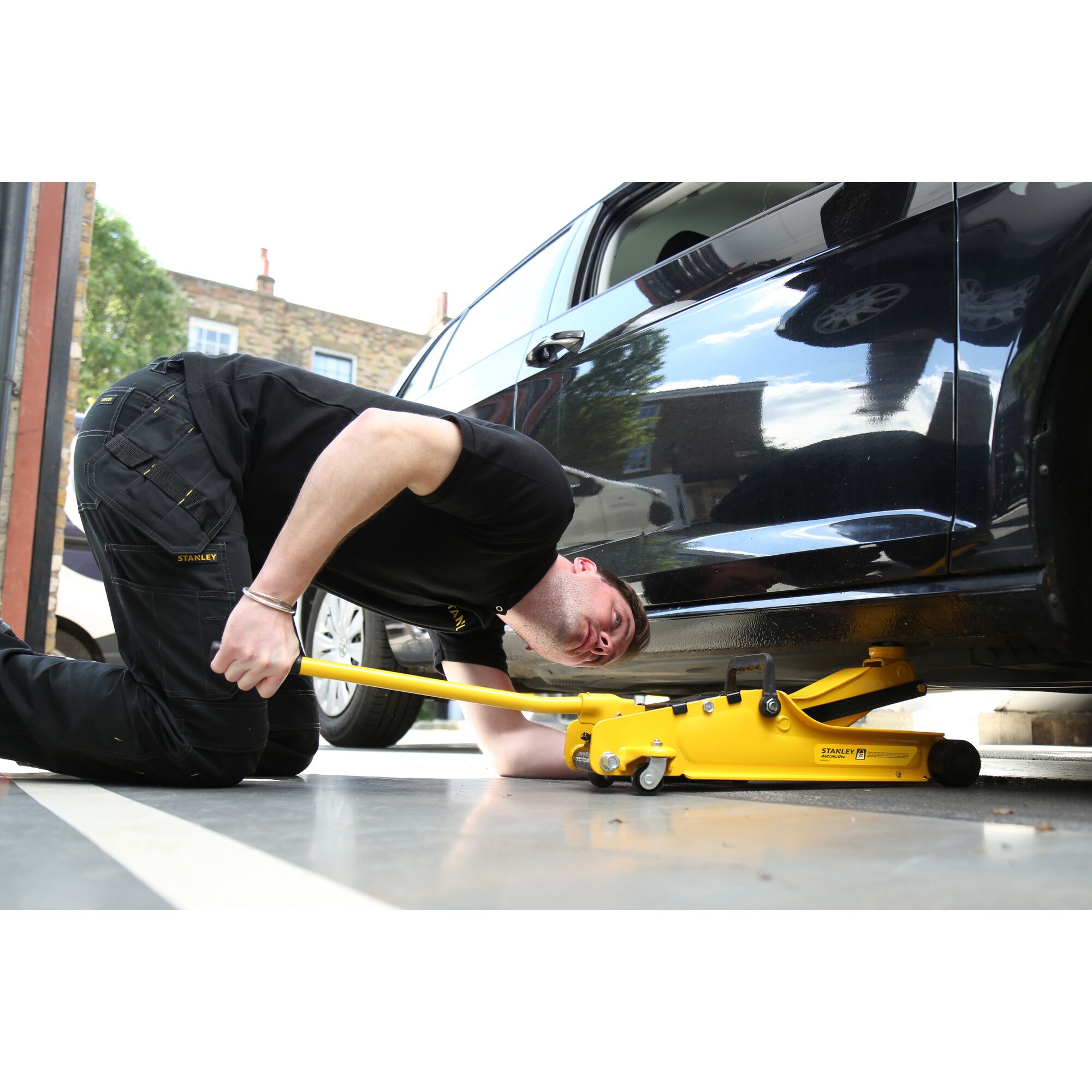 Photo of STANLEY STMT81251-1 hydraulic floor jack in use, lifting a black car by its side.
