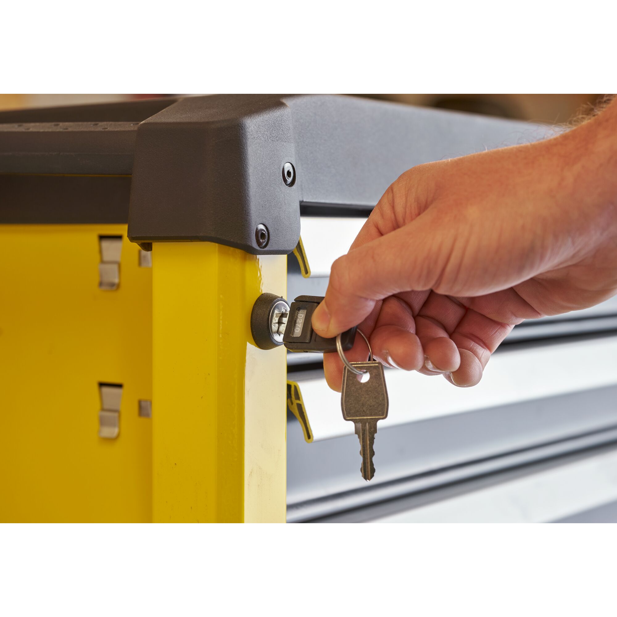 Photo of a hand locking a yellow STANLEY STST74305-1 tool chest with a key, close-up side view.